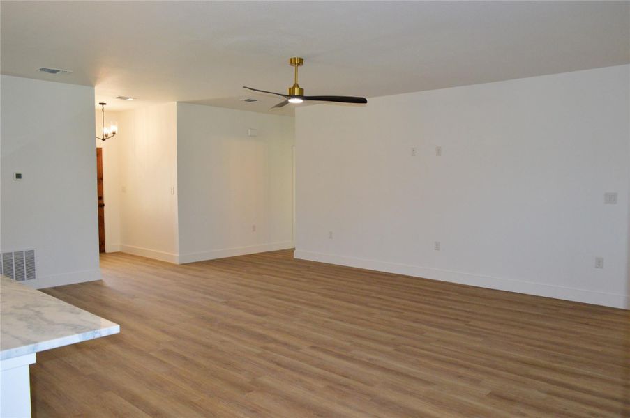 Unfurnished living room with light wood-type flooring, a chandelier, and ceiling fan Unfurnished living room with light wood-type flooring, a chandelier, and ceiling fan