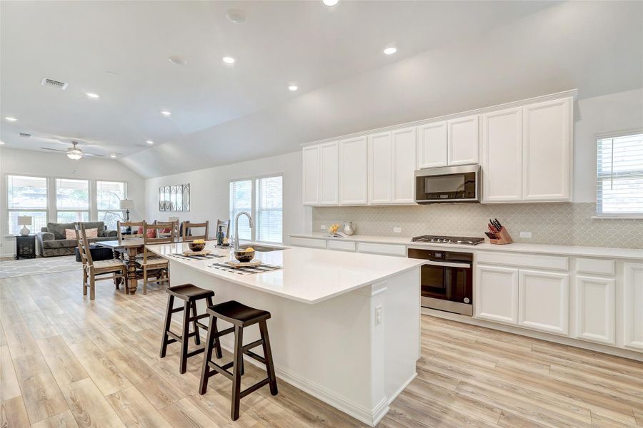 Kitchen with stainless steel appliances, lofted ceiling, an island with sink, light wood-type flooring, and tasteful backsplash