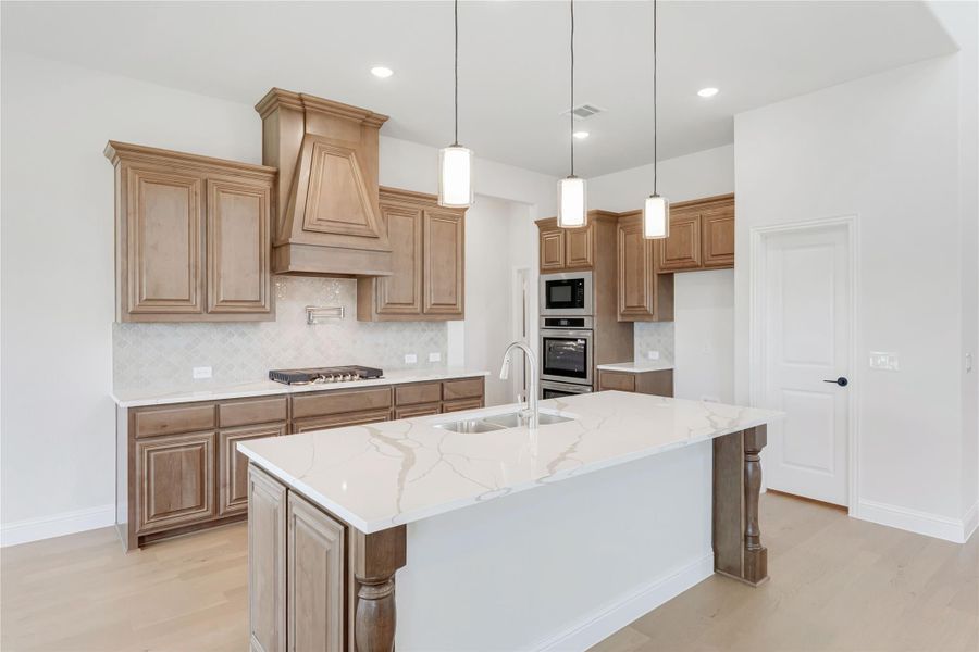 Kitchen with large quartz island, wood cabinets, custom range hood, and stainless steel appliances Kitchen with large quartz island, wood cabinets, custom range hood, and stainless steel appliances