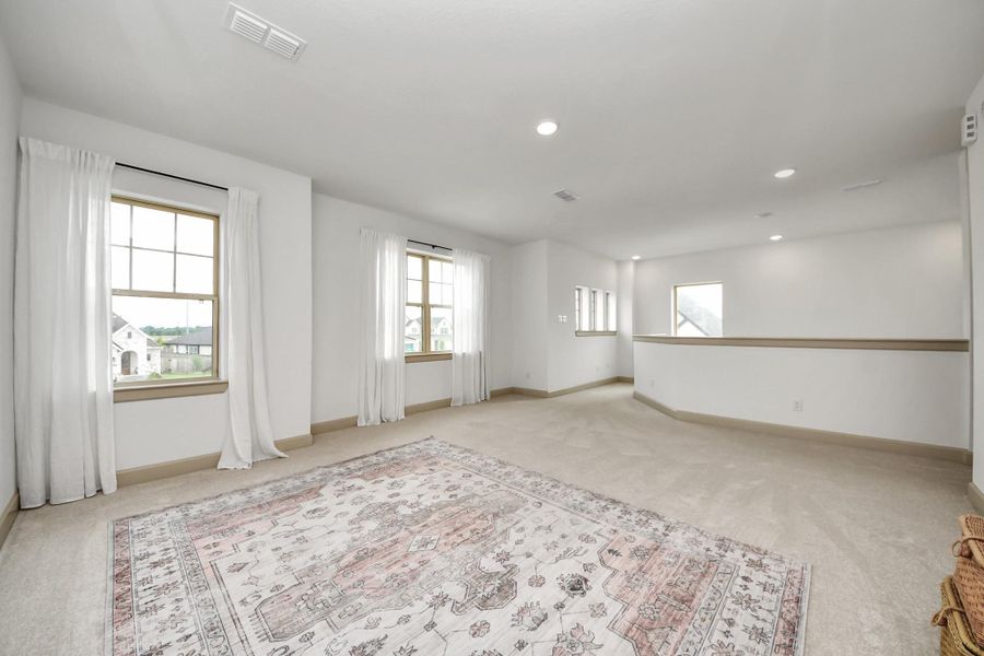 This spacious, bright room features large windows with elegant drapes, soft carpet flooring, and recessed lighting, creating a welcoming atmosphere. Ideal for a living area or entertainment space.
