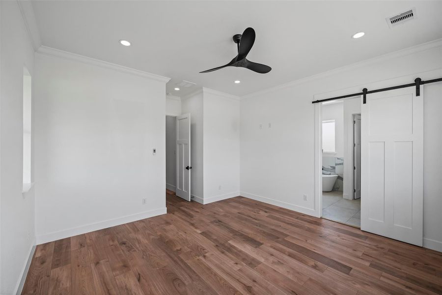 Spacious primary bedroom featuring elegant LVP floors, modern ceiling fan, and convenient ensuite access with a stylish sliding barn door.