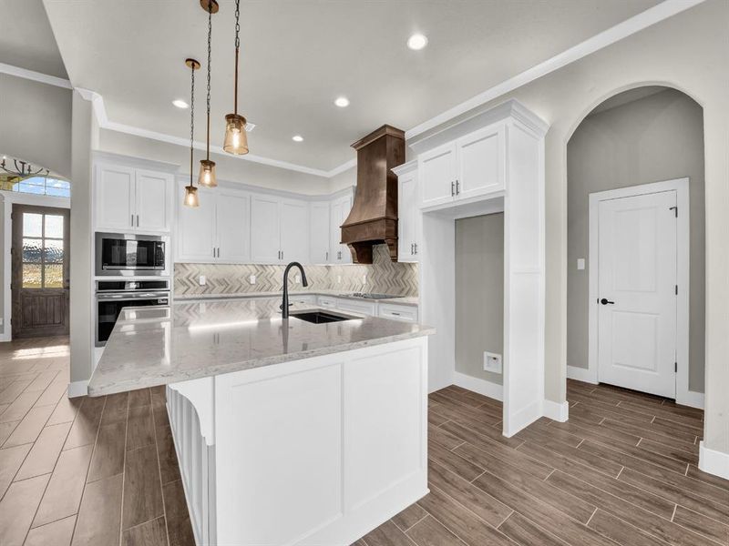 Kitchen with decorative backsplash, a kitchen island with sink, white cabinetry, decorative light fixtures, and light stone counters Kitchen with decorative backsplash, a kitchen island with sink, white cabinetry, decorative light fixtures, and light stone counters