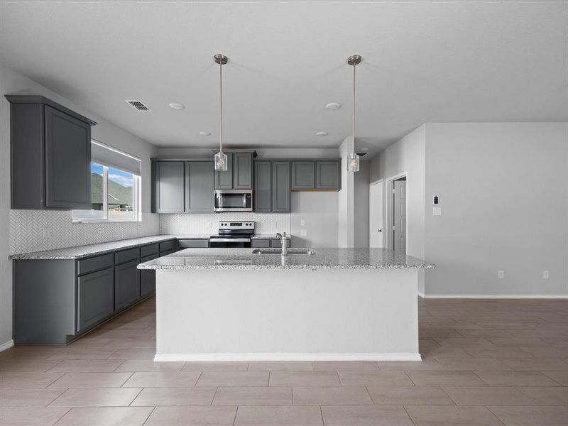 Kitchen featuring gray cabinetry, light stone counters, backsplash, a kitchen island with sink, and stainless steel appliances Kitchen featuring gray cabinetry, light stone counters, backsplash, a kitchen island with sink, and stainless steel appliances