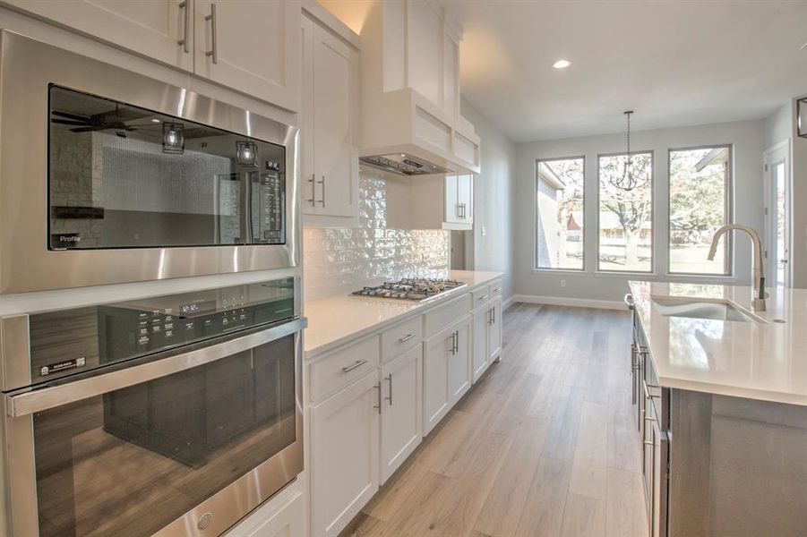 Kitchen featuring appliances with stainless steel finishes, sink, light hardwood / wood-style flooring, white cabinetry, and hanging light fixtures