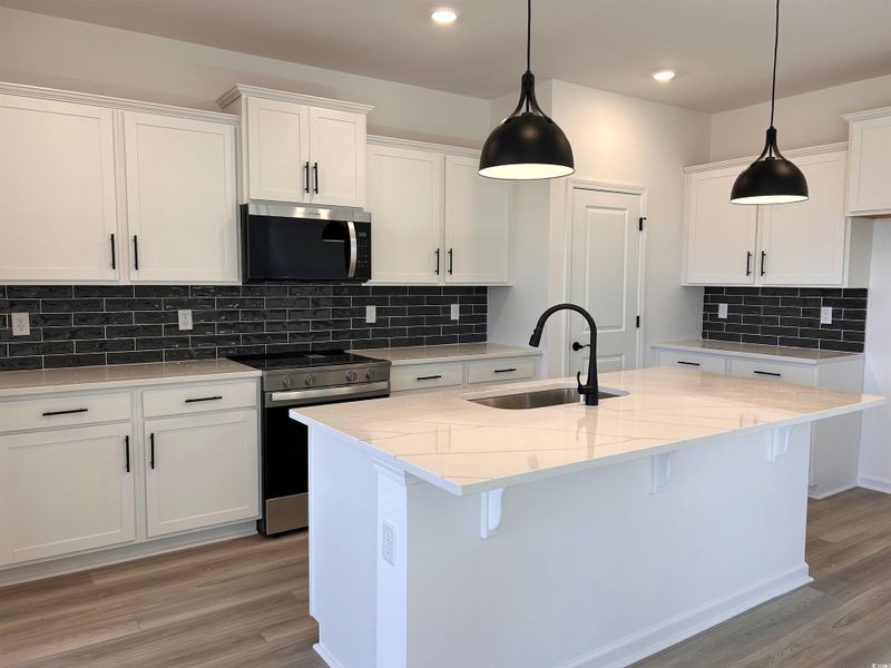 Kitchen with appliances with stainless steel finishes, light stone countertops, a breakfast bar, white cabinetry, and a center island with sink