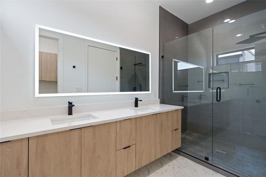 Bathroom with double vanity, marble finish floor, a shower, front lit LED mirror, and dual sinks