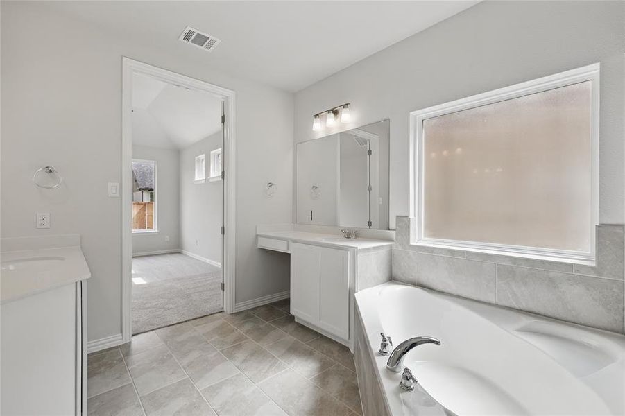 Bathroom featuring two vanities, a bath, and light tile patterned flooring