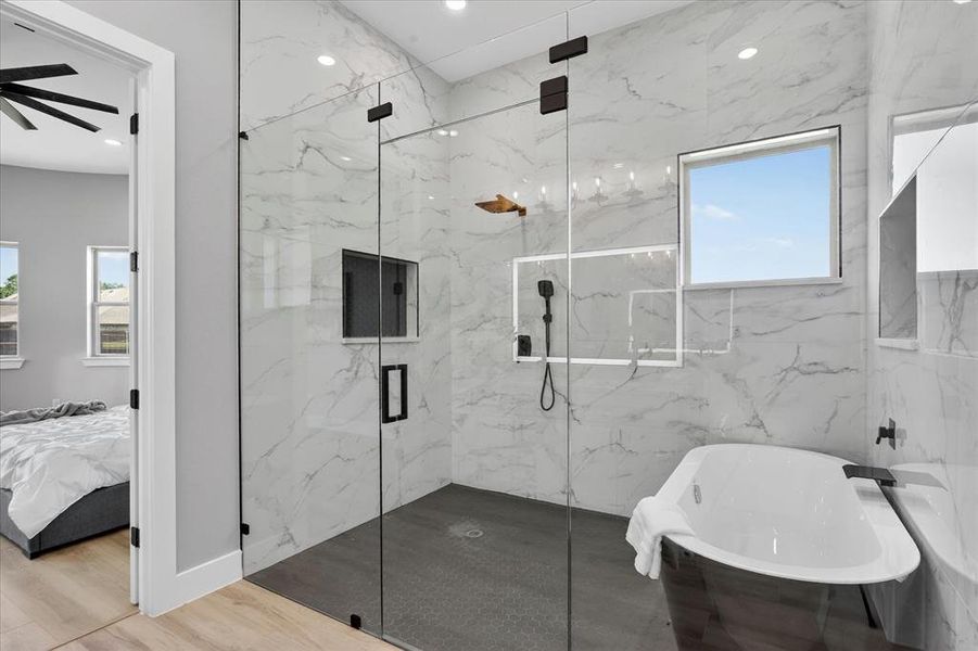 Spacious bathroom featuring a glass-enclosed shower with contrasting dark tile flooring, a freestanding soaking tub, and a window for natural light