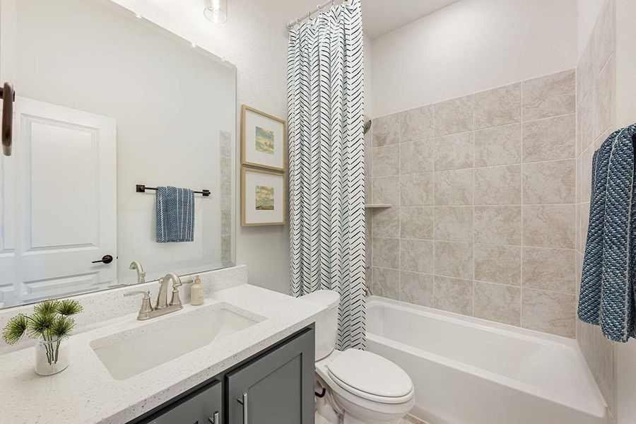 Bathroom with gray vanity, white quartz countertop, and tiled tub-shower combo with curtain