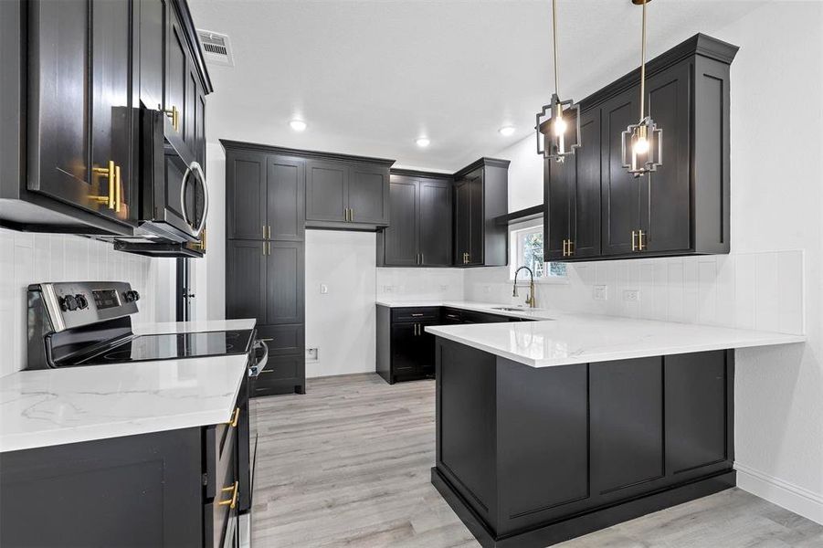 Kitchen featuring backsplash, decorative light fixtures, appliances with stainless steel finishes, light hardwood / wood-style floors, and kitchen peninsula