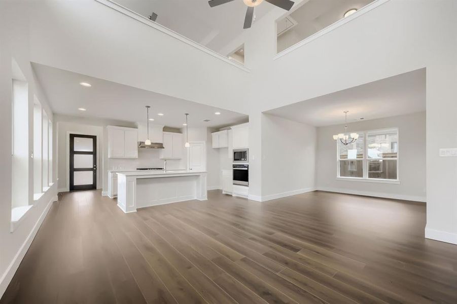 Open-concept living area featuring high ceilings, wood-finish flooring, a contemporary kitchen island, white cabinetry, and built-in stainless steel appliances
