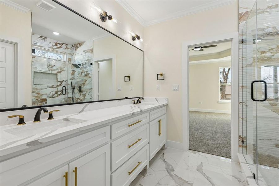 Full bathroom featuring light marble finish flooring, a marble finish shower, ornamental molding, double vanity, and healthy amount of natural light