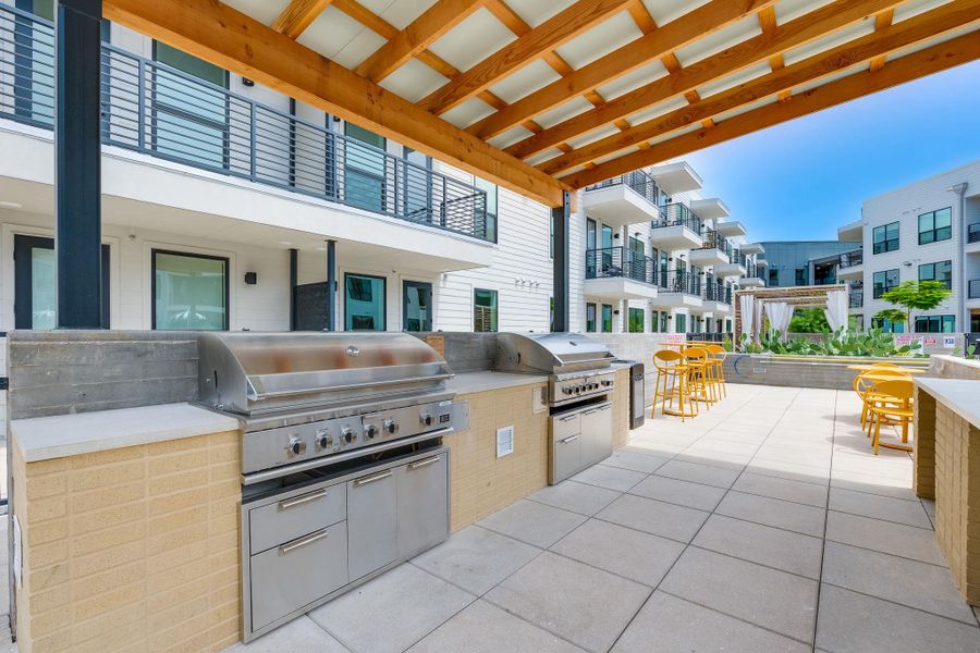 Outdoor kitchen area with two stainless steel grills, a light-toned wood pergola, and a tiled patio
