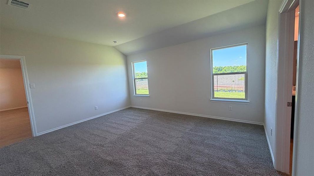 Spacious room featuring vaulted ceilings, plush carpeting, two windows, and neutral wall paint
