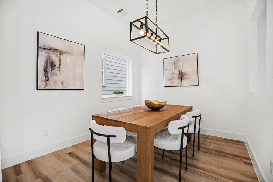 This dining area features a modern design. It has light wood flooring, white walls, and a stylish rectangular light fixture, creating a bright and inviting space.
