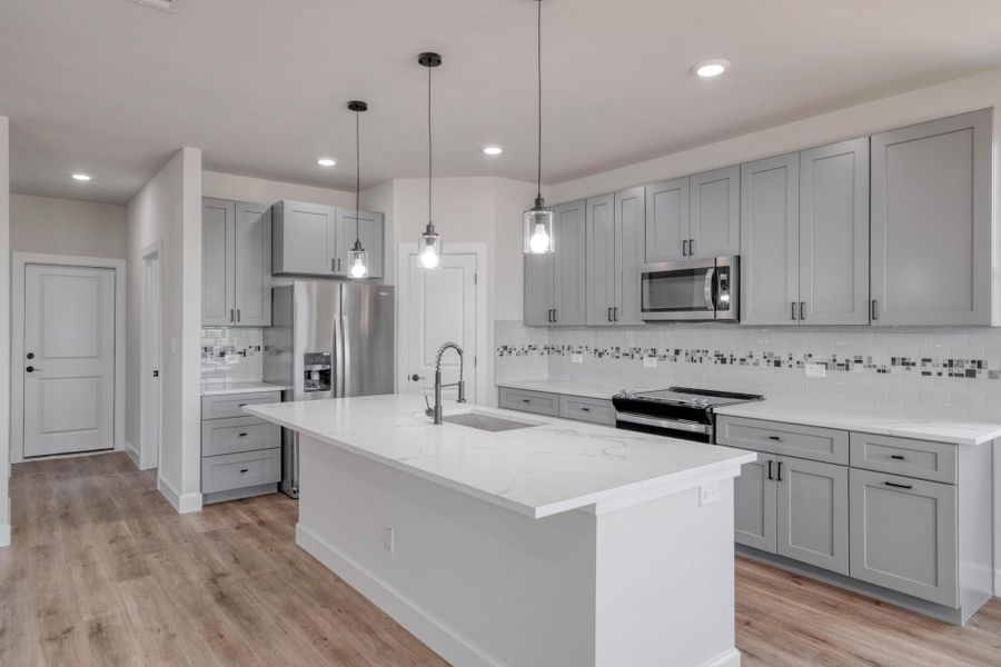 Kitchen with stainless steel appliances, gray cabinets, a sink, light wood finished floors, and backsplash