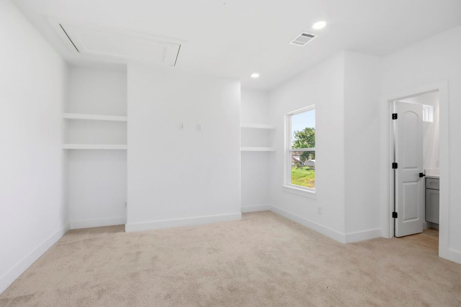 Bright and spacious room featuring plush carpeting, built-in shelves, and a large window for natural light, with easy access to an adjoining room.