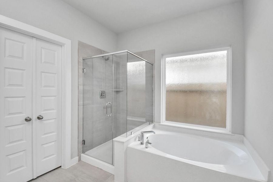 Indulge in a spa-like retreat within the confines of this primary bathroom. Delight in a spacious walk-in shower enveloped in stylish tile surround and unwind in a separate garden tub adorned with custom detailing. Sample photo of completed home with similar floor plan. Actual colors and selections may vary.