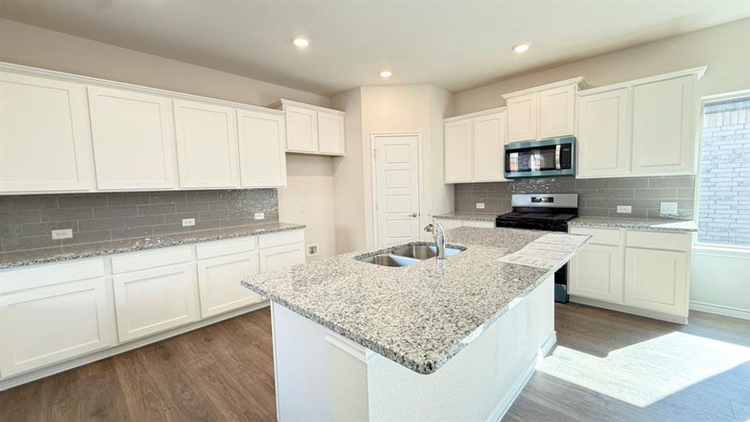 Kitchen with light stone countertops, dark wood-style floors, white cabinetry, stainless steel appliances, and recessed lighting Kitchen with light stone countertops, dark wood-style floors, white cabinetry, stainless steel appliances, and recessed lighting