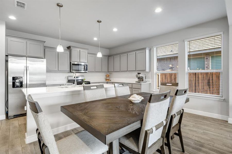 Kitchen with gray cabinets, appliances with stainless steel finishes, light countertops, a kitchen island with sink, and light wood finished floors