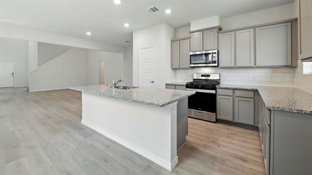 Kitchen with gray cabinetry, stainless steel appliances, an island with sink, light stone countertops, and recessed lighting