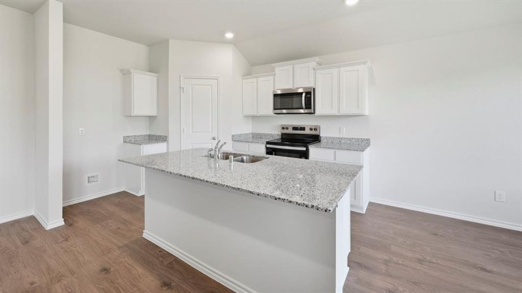 Kitchen with white cabinetry, stainless steel appliances, light stone countertops, an island with sink, and dark wood-style floors Kitchen with white cabinetry, stainless steel appliances, light stone countertops, an island with sink, and dark wood-style floors