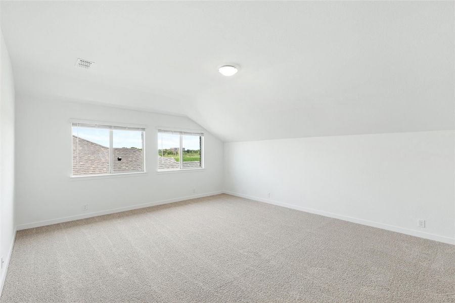 Empty bonus room with vaulted ceiling, carpet flooring, and two windows overlooking neighborhood rooftops