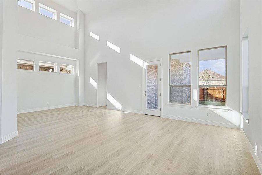 Unfurnished living room with a towering ceiling, light hardwood / wood-style floors, and a wealth of natural light