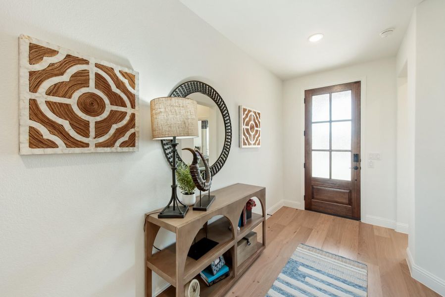 Entryway with wood console table, round mirror, wall art, and wood front door with glass panels on light hardwood floors Entryway with wood console table, round mirror, wall art, and wood front door with glass panels on light hardwood floors