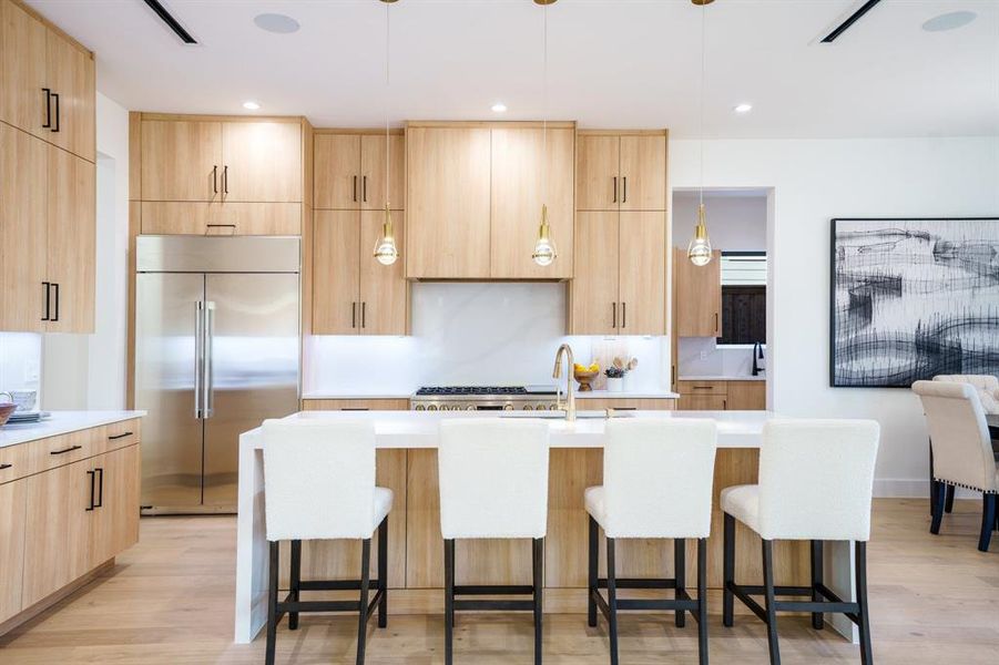 Kitchen featuring stainless steel built in refrigerator, a center island with sink, light brown cabinetry, and pendant lighting