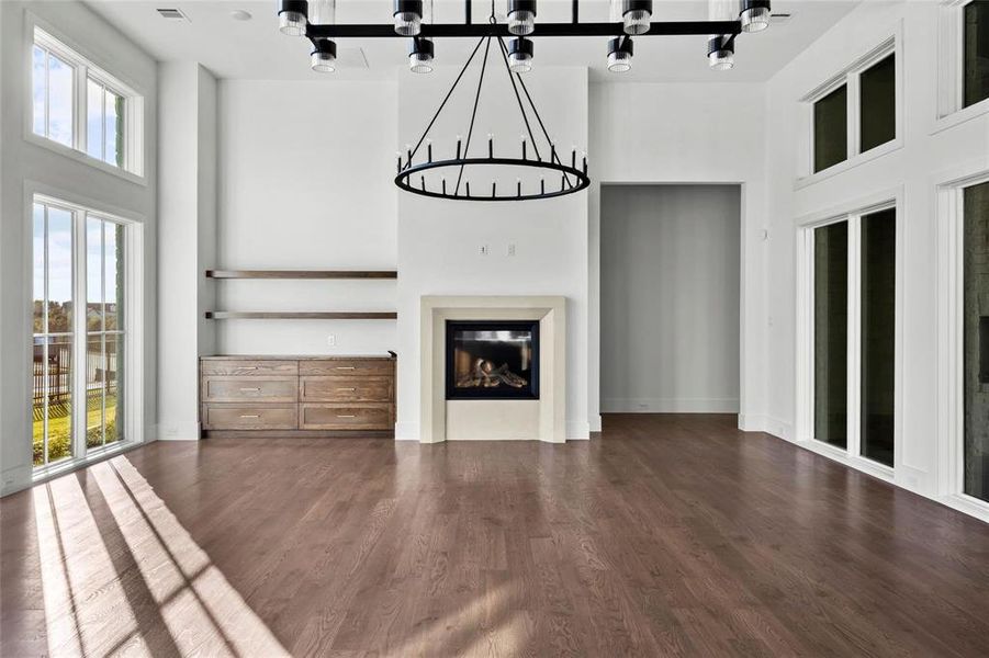 Unfurnished living room featuring a high ceiling, a glass covered fireplace, and dark wood-style flooring Unfurnished living room featuring a high ceiling, a glass covered fireplace, and dark wood-style flooring