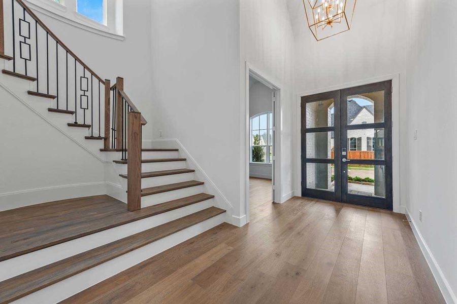 Foyer with hardwood / wood-style flooring, a high ceiling, a notable chandelier, and french doors