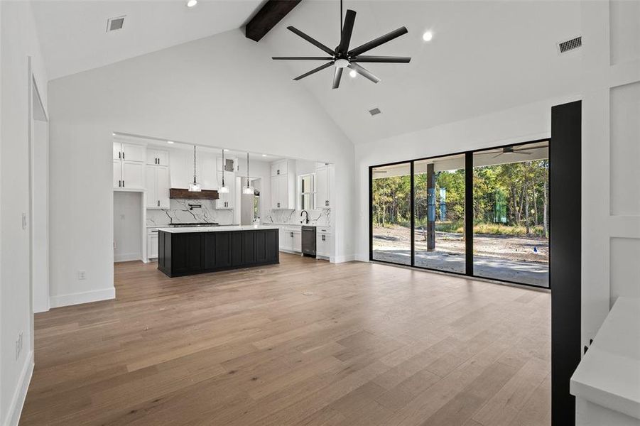 Unfurnished living room featuring beam ceiling, light wood-type flooring, high vaulted ceiling, a ceiling fan, and recessed lighting Unfurnished living room featuring beam ceiling, light wood-type flooring, high vaulted ceiling, a ceiling fan, and recessed lighting