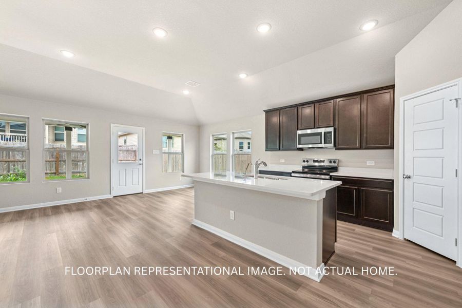 A contemporary kitchen and living area featuring dark cabinetry, bright white countertops, and ample natural light.