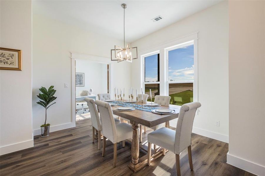Sun-drenched dining room with sweeping pastoral views through expansive windows. Statement lighting fixture illuminates the dedicated dining space perfect for gathering and entertaining.