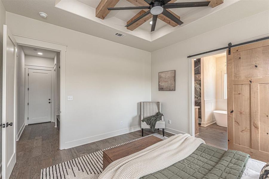 Bedroom featuring a barn door, wood finished floors, a ceiling fan, ensuite bathroom, and a tray ceiling