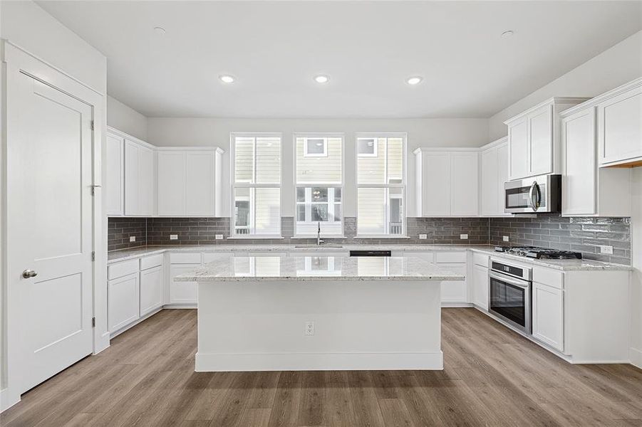 The kitchen features white cabinetry, a large island with a light-colored countertop, and a tiled backsplash