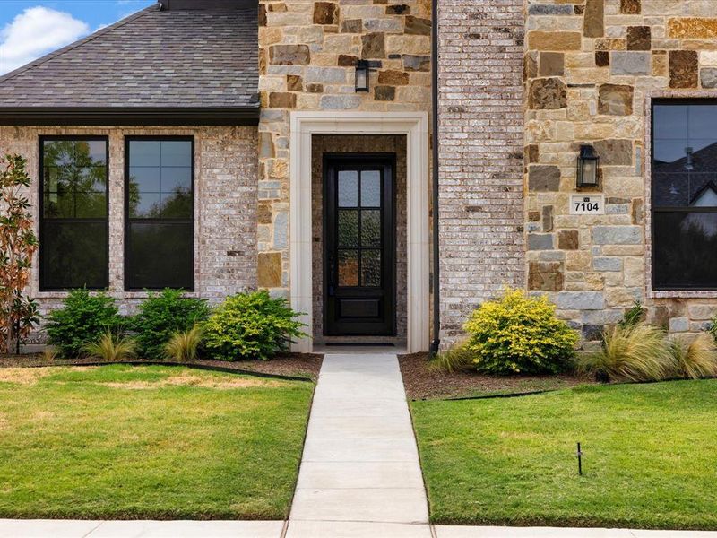 Doorway to property featuring stone siding, a yard, and a shingled roof