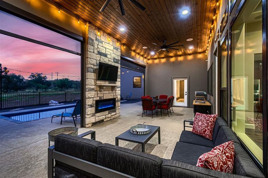 The covered patio features an electric fireplace and industrial power screens that open to the beautiful swimming pool.