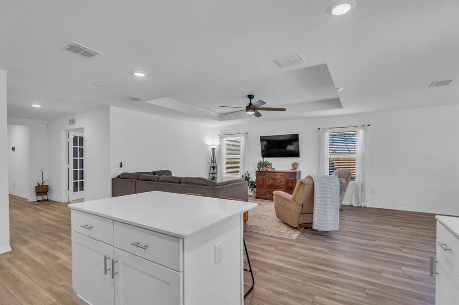Kitchen with a tray ceiling, open floor plan, white cabinets, light wood-style floors, and recessed lighting