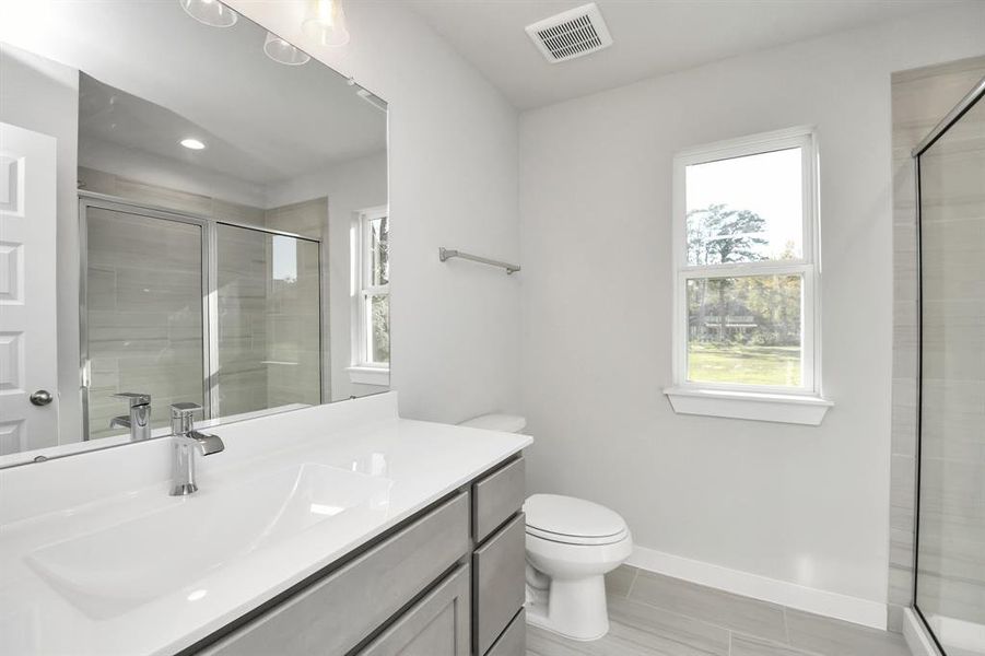 Secondary bath features tile flooring, walk-in shower with tile surround, light stainedwood cabinets, beautiful light countertop.