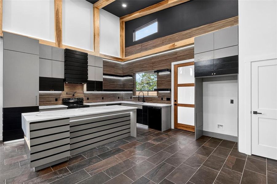 Kitchen featuring light stone counters, a high ceiling, a center island, black appliances, and modern cabinets Kitchen featuring light stone counters, a high ceiling, a center island, black appliances, and modern cabinets
