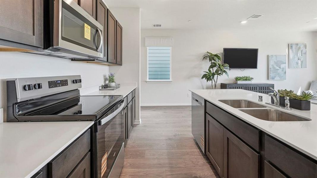 Kitchen featuring appliances with stainless steel finishes, dark brown cabinetry, light wood-type flooring, light stone countertops, and recessed lighting Kitchen featuring appliances with stainless steel finishes, dark brown cabinetry, light wood-type flooring, light stone countertops, and recessed lighting