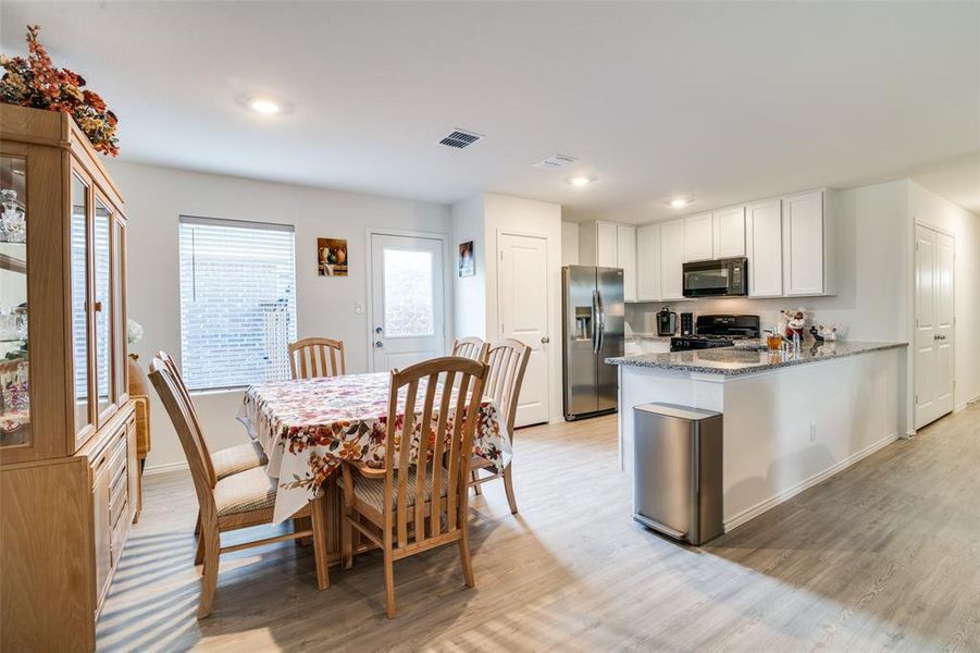 Kitchen featuring white cabinetry, light hardwood / wood-style flooring, stone countertops, and black appliances