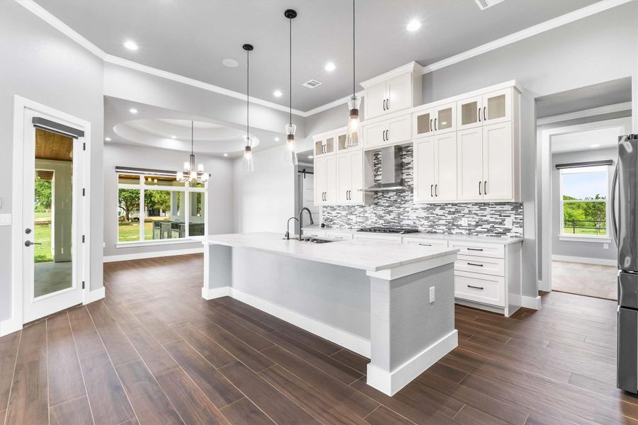 Kitchen featuring a sink, wall chimney range hood, baseboards, crown molding, and healthy amount of natural light Kitchen featuring a sink, wall chimney range hood, baseboards, crown molding, and healthy amount of natural light