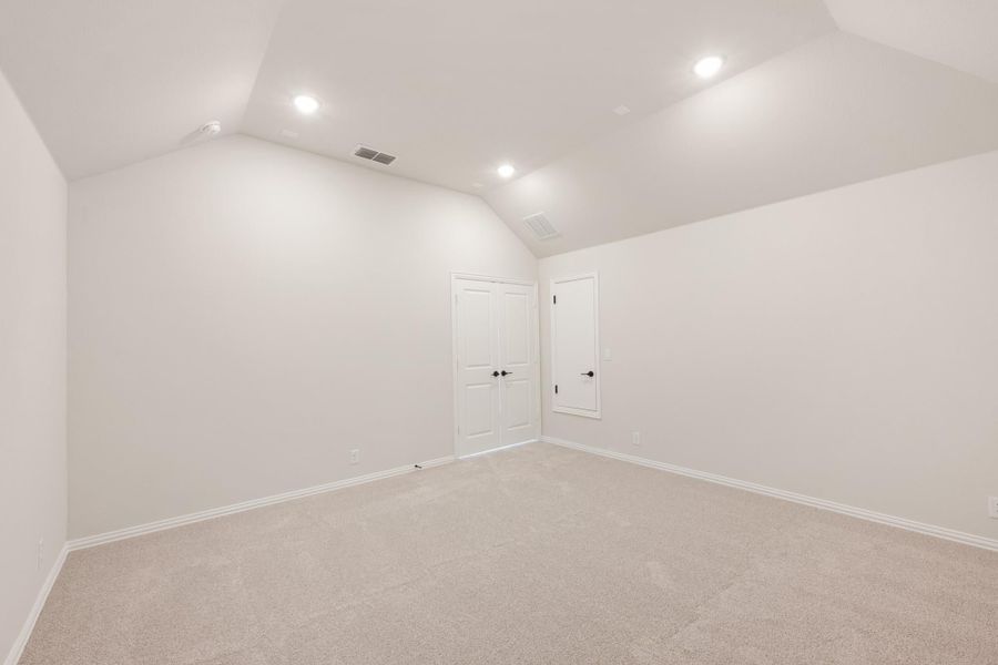 Empty bedroom with vaulted ceiling, carpet flooring, recessed lighting, and two white doors Empty bedroom with vaulted ceiling, carpet flooring, recessed lighting, and two white doors