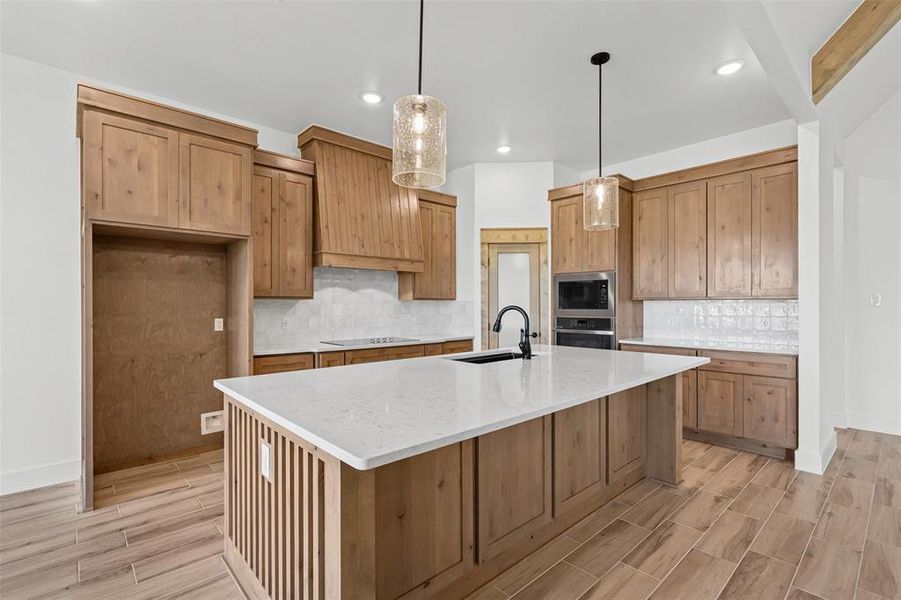 Kitchen featuring light stone counters, wood finish floors, tasteful backsplash, decorative light fixtures, and appliances with stainless steel finishes
