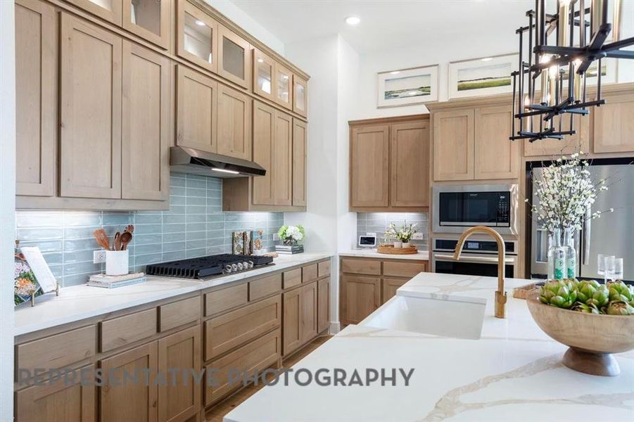 Kitchen featuring pendant lighting, decorative backsplash, stainless steel appliances, light stone countertops, and glass insert cabinets