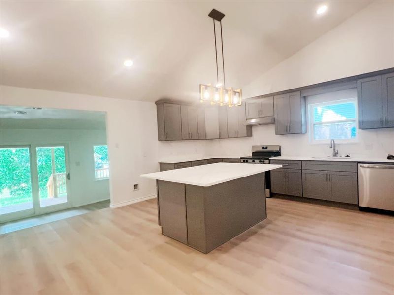 Kitchen featuring an island with a white countertop, gray cabinetry, stainless steel appliances, and wood-finish flooring