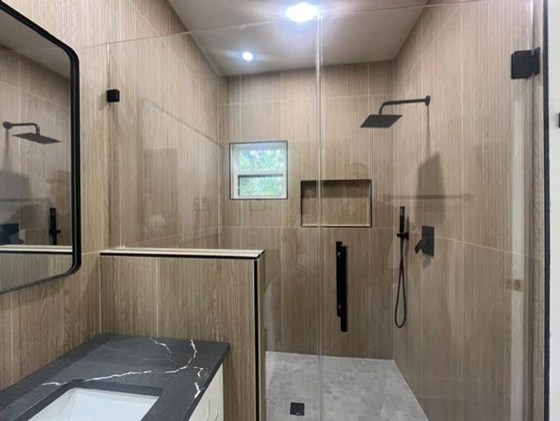 Modern bathroom featuring a glass-enclosed shower with matte black fixtures, a built-in shower niche, and light-toned wood-look tile Modern bathroom featuring a glass-enclosed shower with matte black fixtures, a built-in shower niche, and light-toned wood-look tile